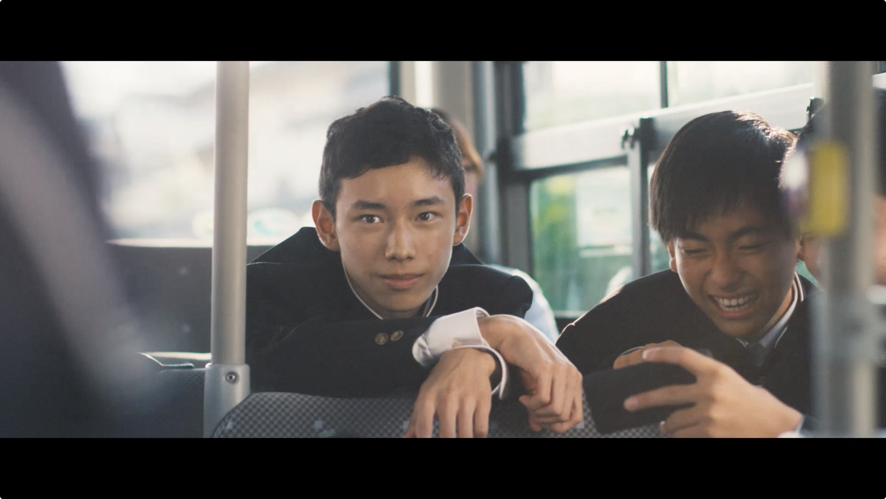 バスの座席でスマートフォンを見ながら笑いあう男子中学生。
